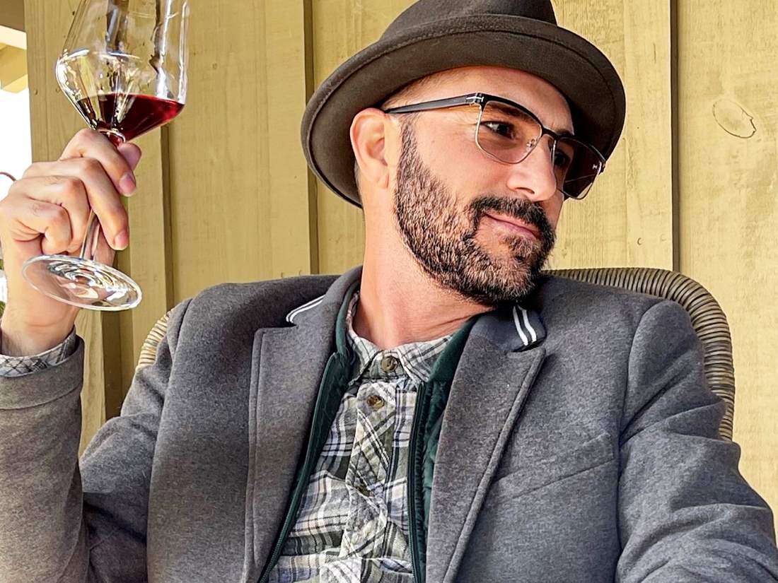 Man wearing glasses and a hat with a glass of red wine